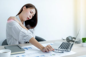 A successful business woman sitting in the office using a laptop to work so hard that it hurts her shoulder