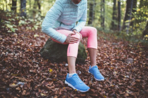 Woman sitting outside in the woods on a rock holding her knee in pain