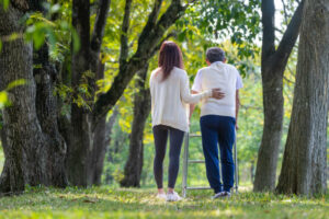 Asian senior father with walker and daughter walking together in the park during summer for light exercise and physical therapy