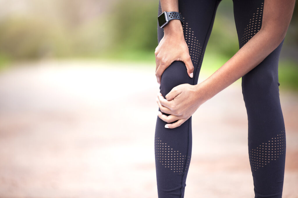 woman experiencing knee pain while exercising outdoors