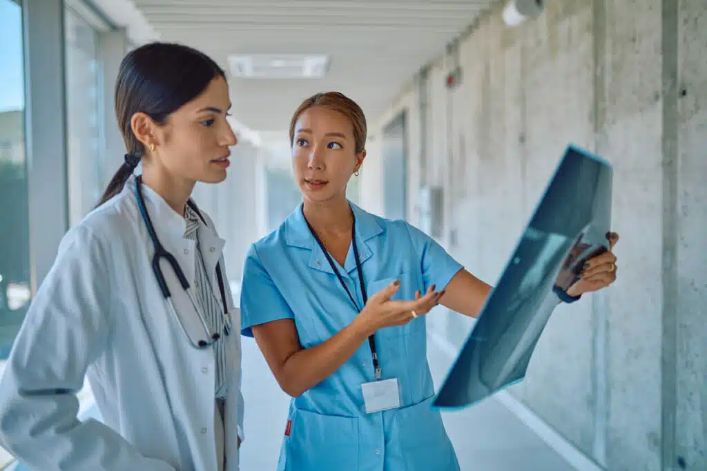 Two female osteoporosis specialists are examining a patient's X-ray during an osteoporosis diagnosis in a hospital corridor.