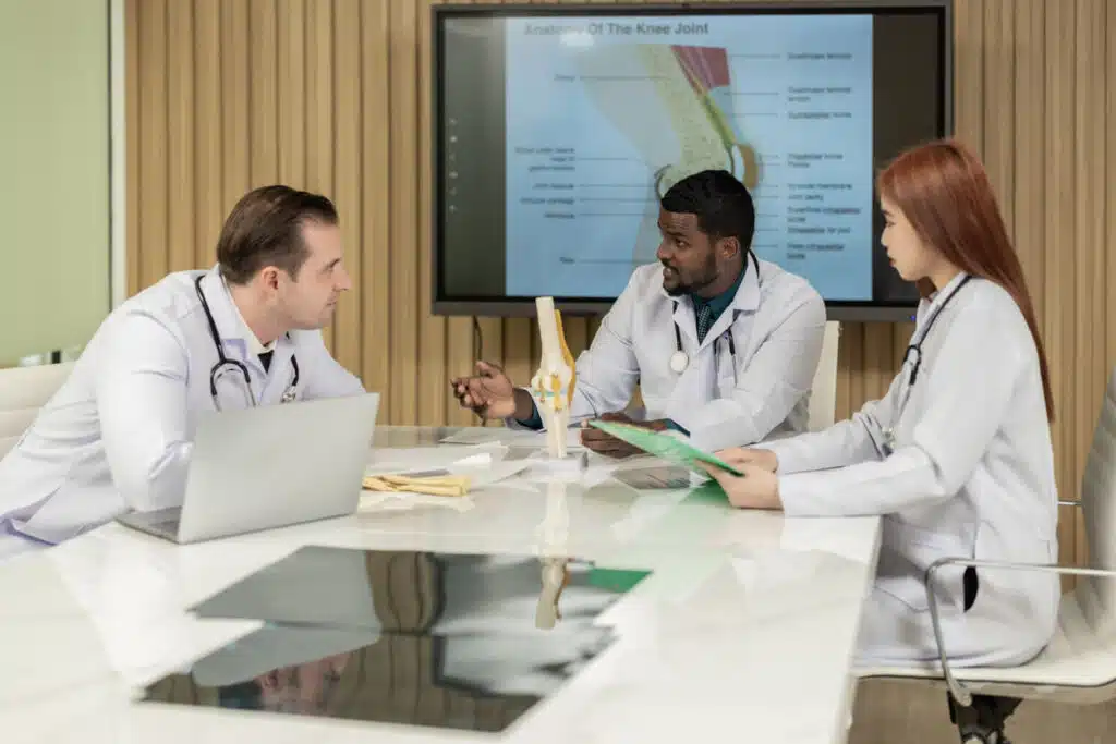 A group of knee replacement surgeons and radiologists discusses a patient's knee joint MRI and plans for further procedures.